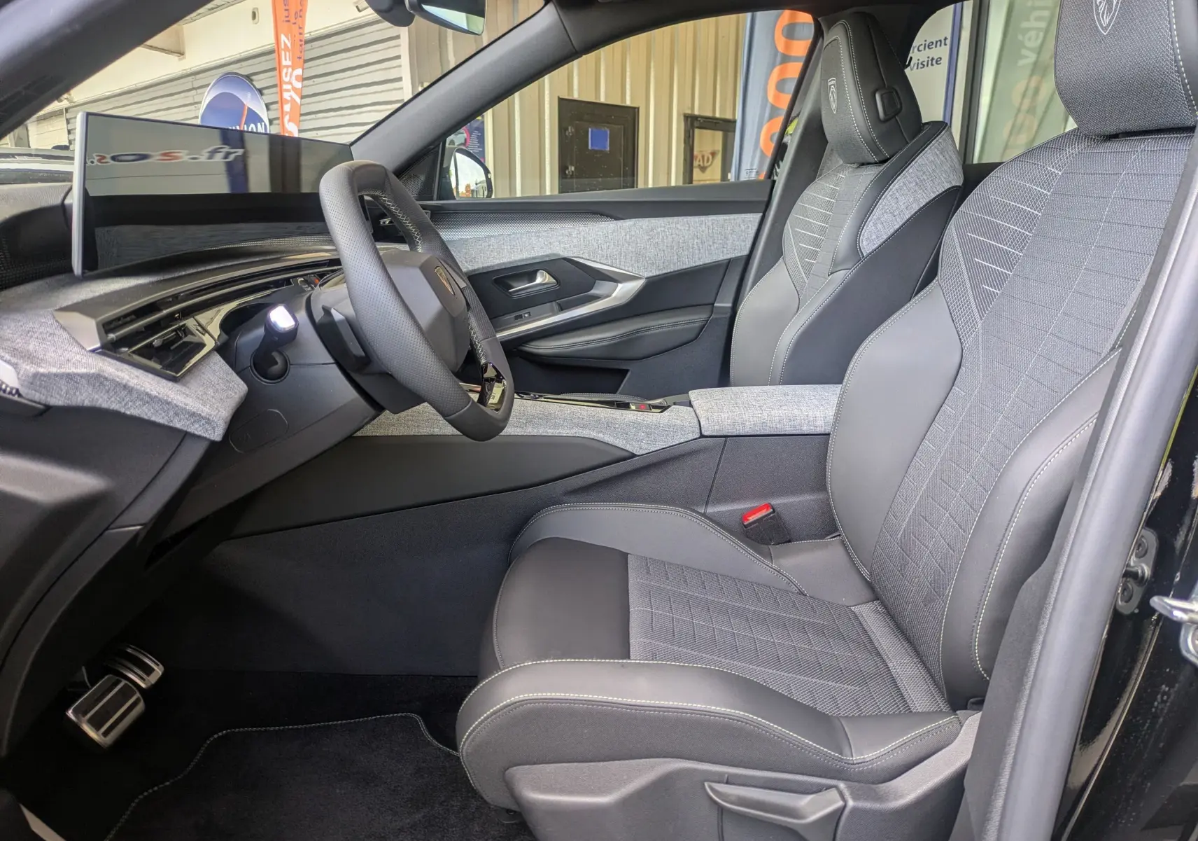 Intérieur côté conducteur du Peugeot 3008 Hybrid 145 GT 2025, sellerie tissu gris avec surpiqûres Iced Clay et tableau de bord moderne.