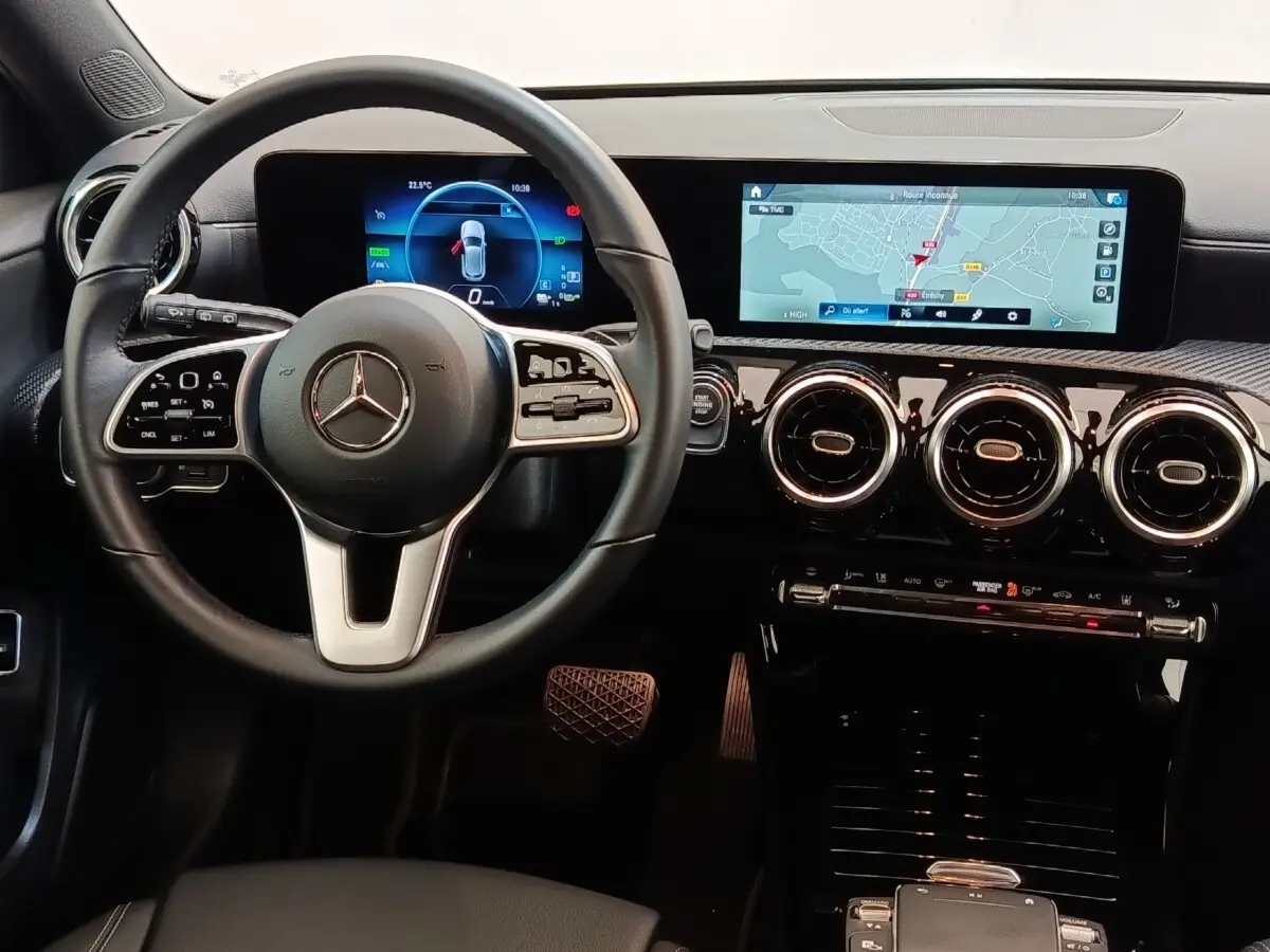 Vue intérieure centrée sur le volant cuir noir et le tableau de bord avec écran tactile et navigation 3D de la Mercedes Classe A.