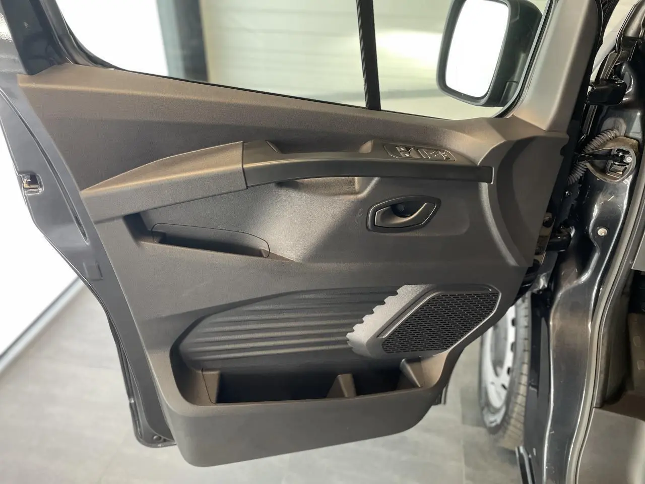 Porte côté conducteur ouverte du Renault Trafic Fourgon gris Comète, montrant les commandes de vitres et le haut-parleur intégré.