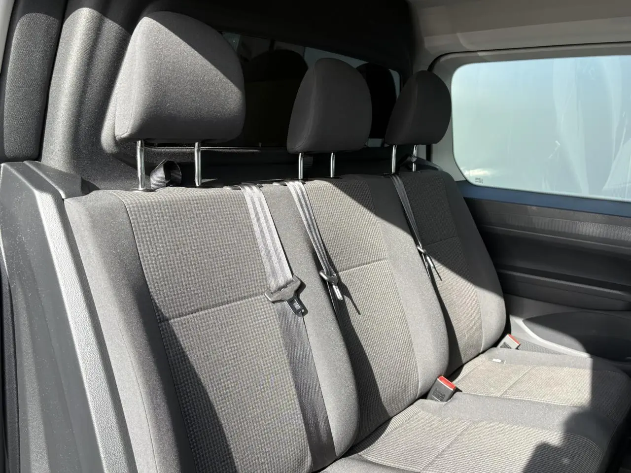 Vue intérieure côté droit montrant la banquette arrière grise avec trois appuie-têtes et ceintures de sécurité du Volkswagen Caddy 2024.