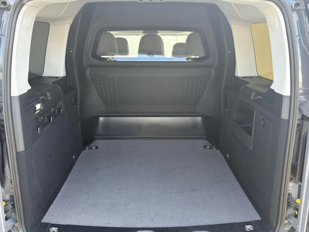 Vue intérieure arrière du coffre spacieux du Volkswagen Caddy Pure Grey 2024, montrant la cloison de séparation et les finitions noires.