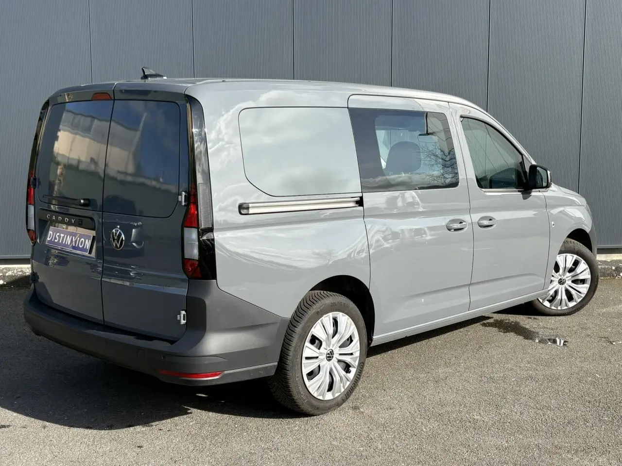 Vue 3/4 arrière droite d’un Volkswagen Caddy 2024 gris Pure Grey avec portes arrière battantes tôlées et porte latérale coulissante.