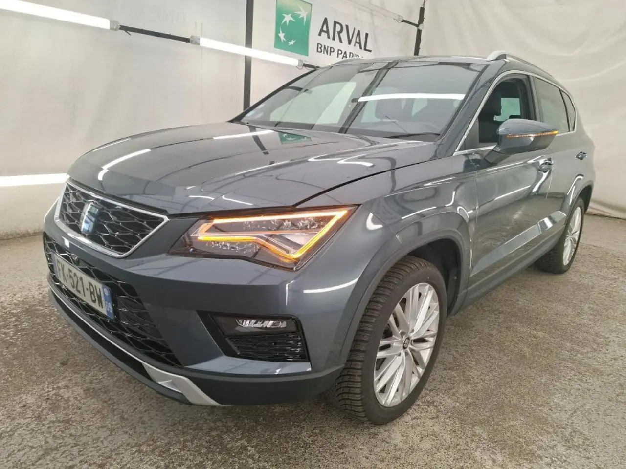 SEAT Ateca gris clair en 3/4 avant droit avec phares LED allumés et jantes alliage 18 pouces visibles.