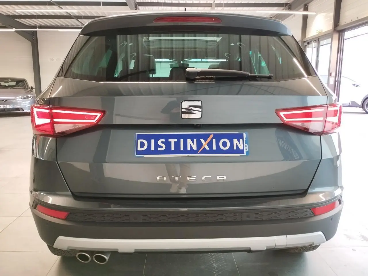 Vue arrière d'un SEAT Ateca gris clair avec double sortie d'échappement et feux arrière LED allumés dans un garage.