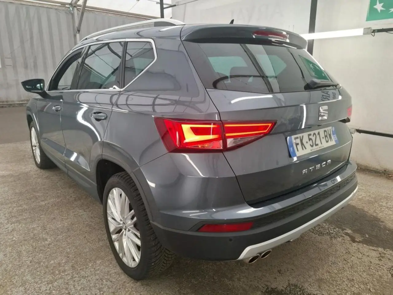 Vue 3/4 arrière droite d'un SEAT Ateca gris clair avec feux arrière LED allumés et double sortie d'échappement chromée.