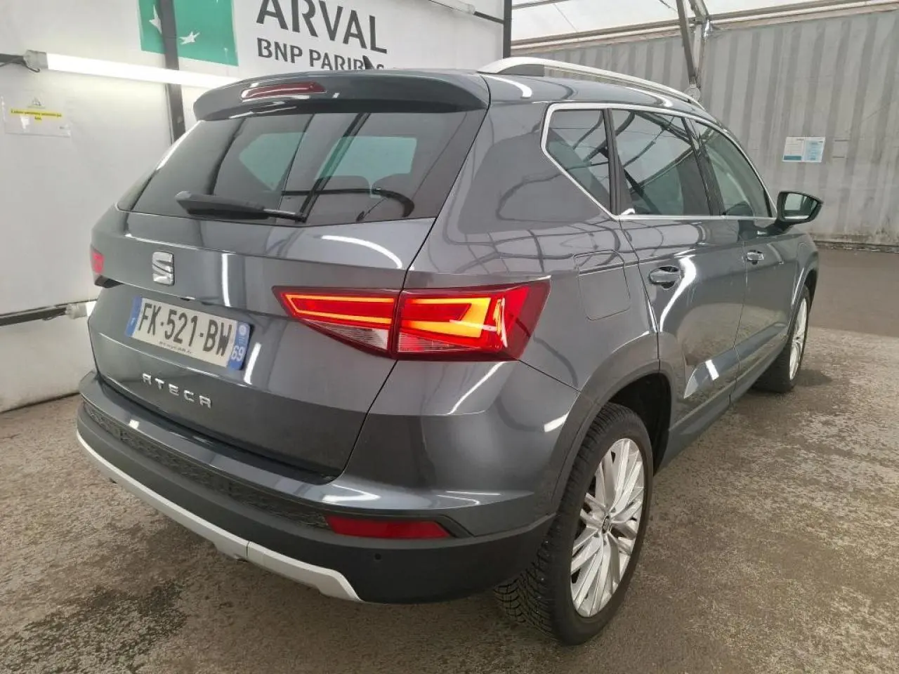 Vue 3/4 arrière droite d'un SEAT Ateca gris clair avec feux arrière LED allumés et jantes alliage 18 pouces.