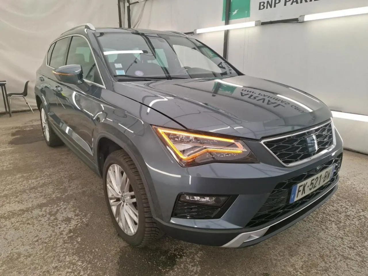 Vue 3/4 avant droit d'un SEAT Ateca gris clair avec phares LED allumés dans un garage intérieur.