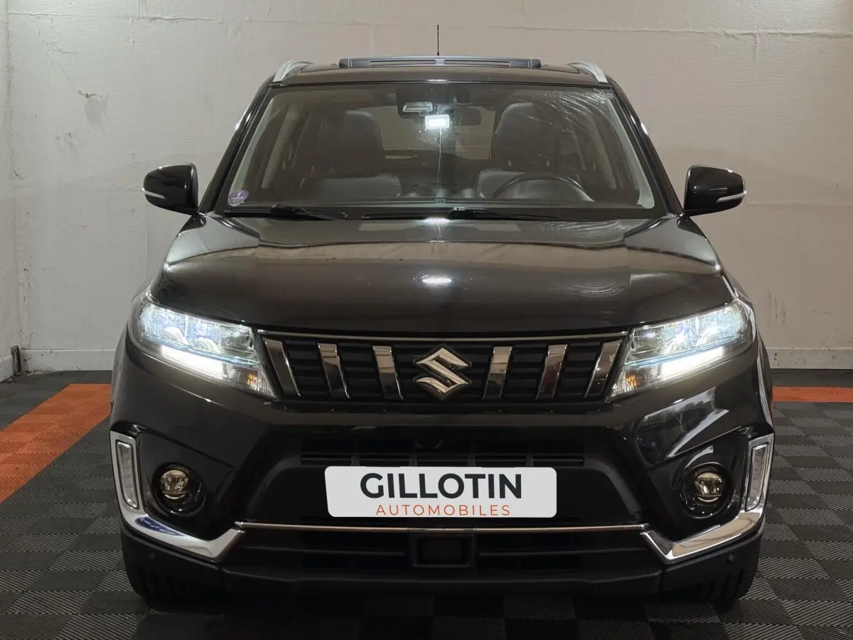Vue frontale d'un Suzuki Vitara noir 2022 avec phares LED allumés et détails chromés sur le pare-chocs.