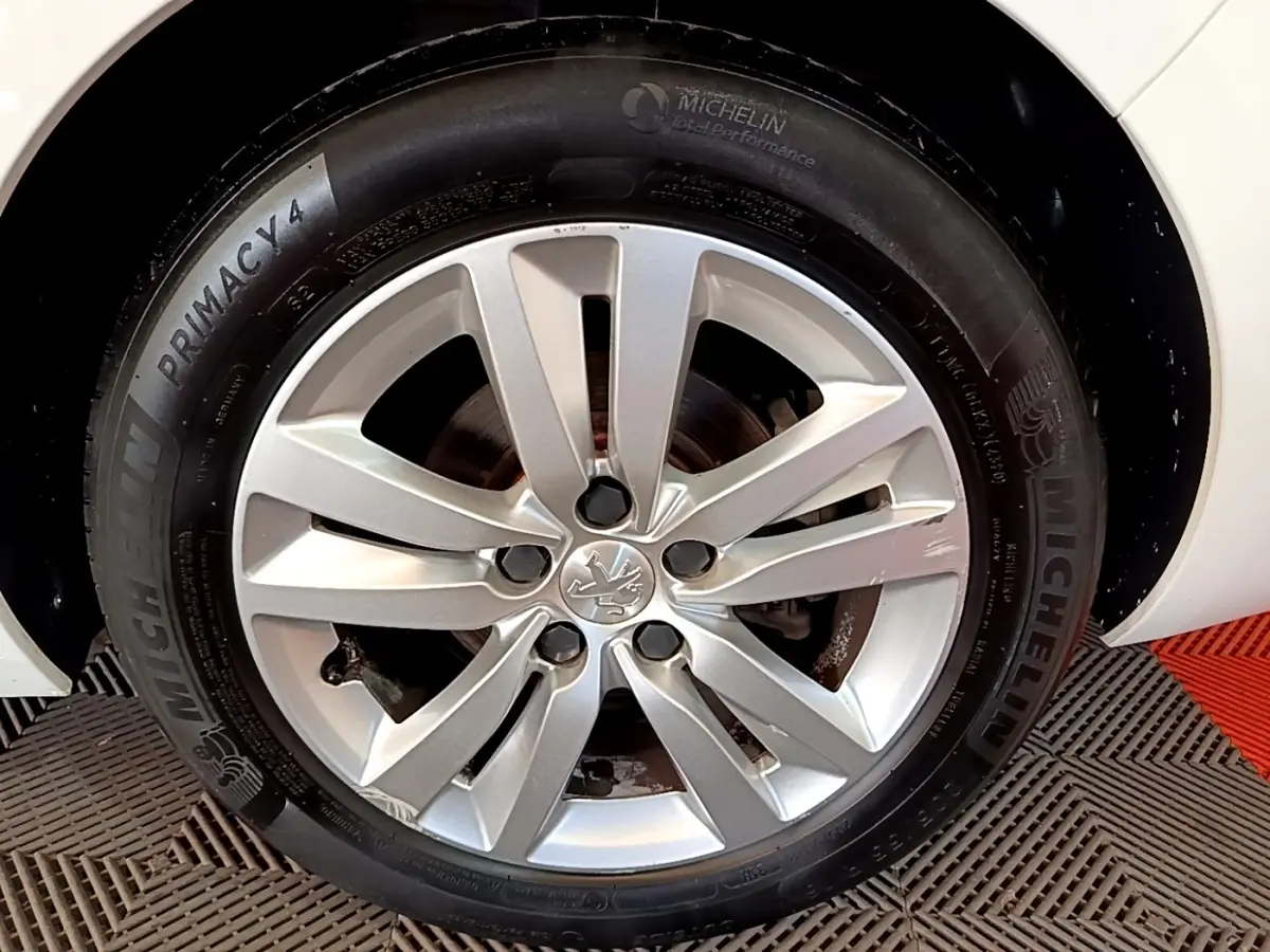 Gros plan sur la roue avant droite d’une Peugeot 308 blanche, jante alliage argent avec logo Peugeot central.