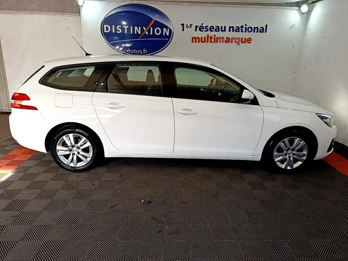 Peugeot 308 break blanc vue de profil côté gauche, avec jantes alliage et rétroviseurs blancs dans un showroom.