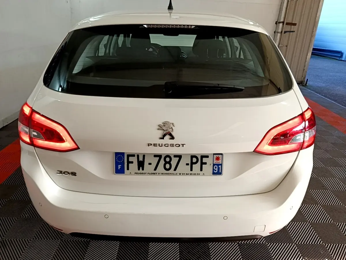 Vue arrière d’une Peugeot 308 blanche avec feux allumés et plaque d’immatriculation française visible.