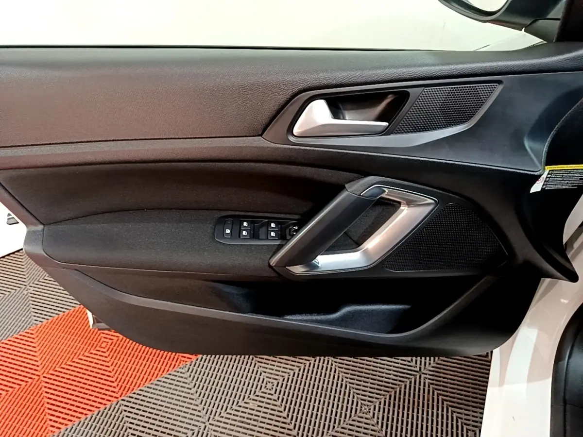 Vue intérieure côté gauche de la porte avant d'une Peugeot 308 blanche, avec commandes électriques et poignée argentée.