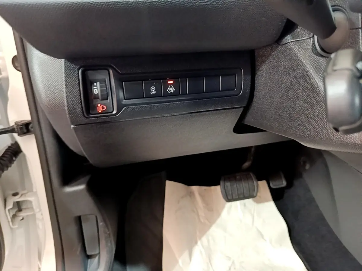 Vue intérieure côté conducteur montrant les commandes d'éclairage et d'assistance sur fond noir, Peugeot 308 blanc visible à l'ouverture.