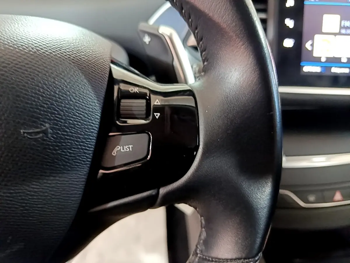 Gros plan sur le volant cuir noir de la Peugeot 308 avec commandes multifonctions et écran tactile partiellement visible.