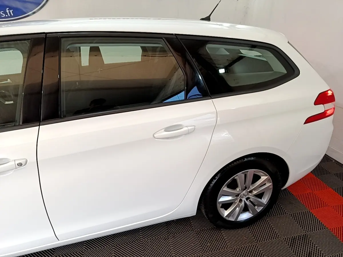 Vue latérale droite d'une Peugeot 308 break blanche, mettant en valeur la porte arrière et la roue arrière.