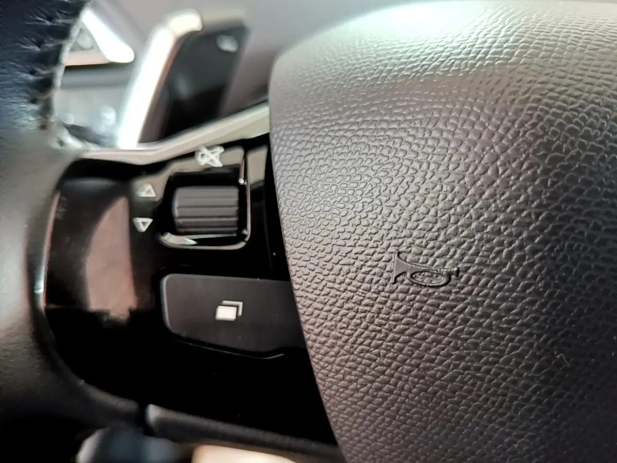 Gros plan sur le volant en cuir noir de la Peugeot 308, avec commandes intégrées et bouton de klaxon visible.