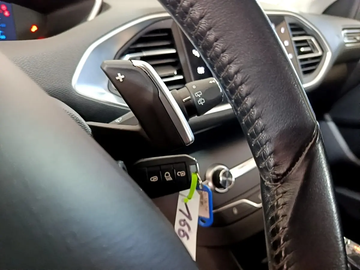 Gros plan intérieur sur le volant cuir noir et la commande de boîte auto de la Peugeot 308 blanche, avec clé et tableau de bord partiel.