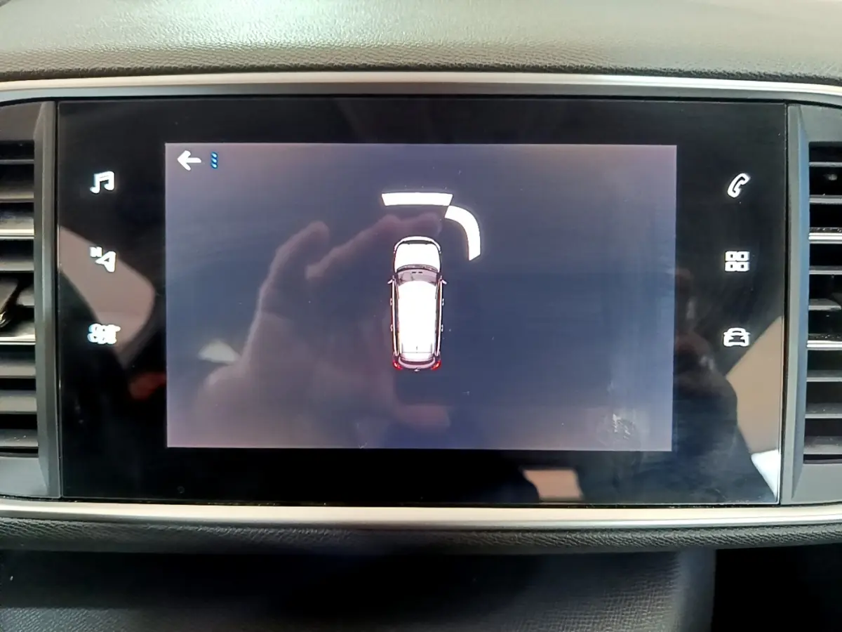Écran tactile central montrant l’alerte de proximité arrière d’une Peugeot 308 blanche, vue intérieure.