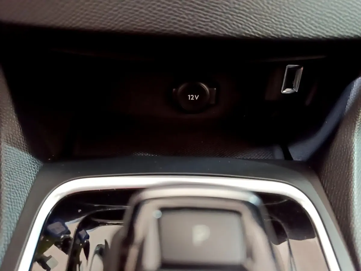 Gros plan sur la console centrale noire de la Peugeot 308 blanche, avec prise 12V et port USB visibles.