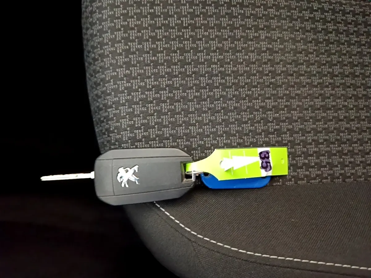 Gros plan sur la clé noire Peugeot posée sur un siège tissu gris à motifs avec étiquette verte numérotée 35.