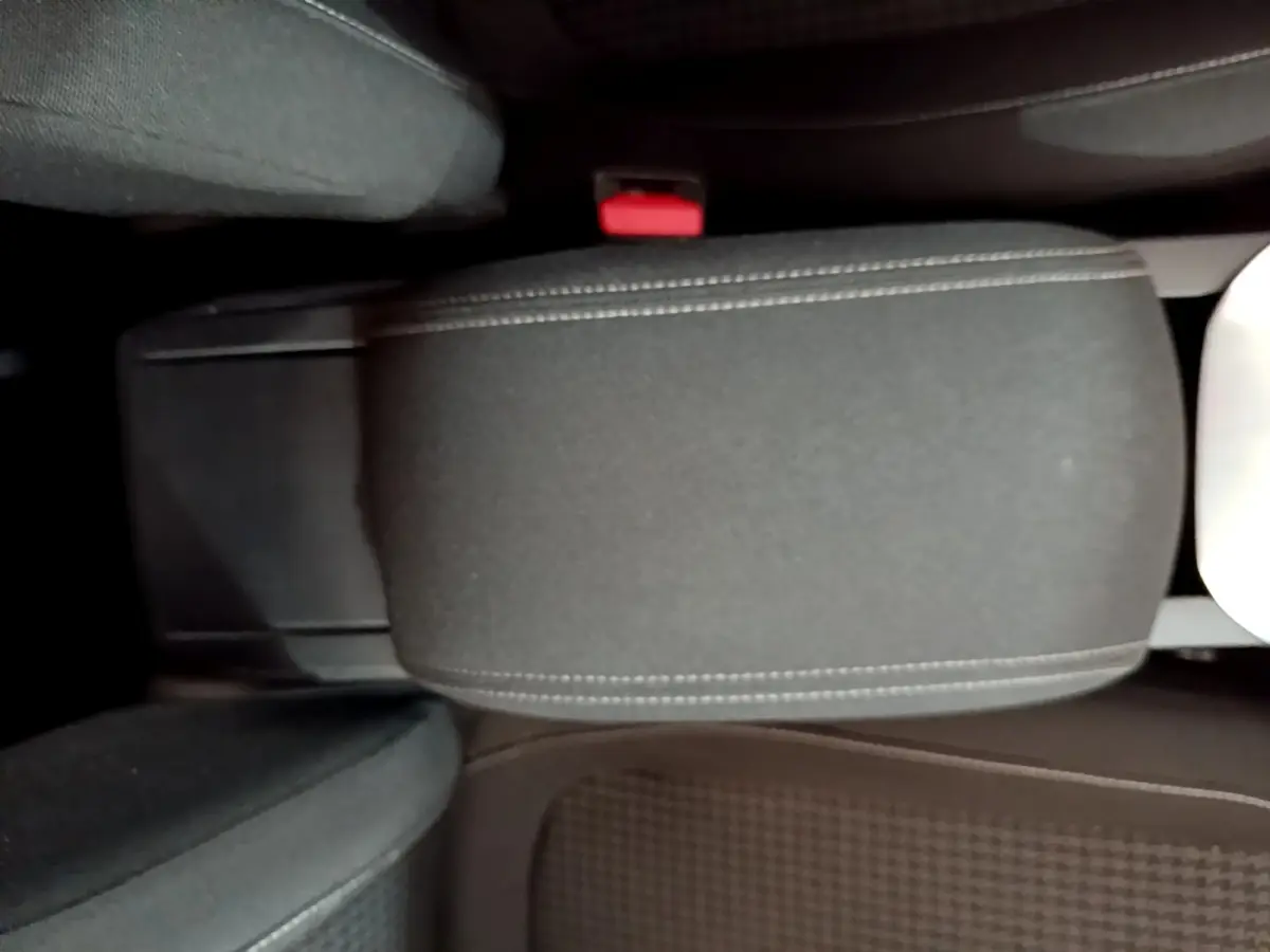 Vue rapprochée de l'accoudoir central noir et des sièges avant tissu dans l'habitacle d'une Peugeot 308 blanche.