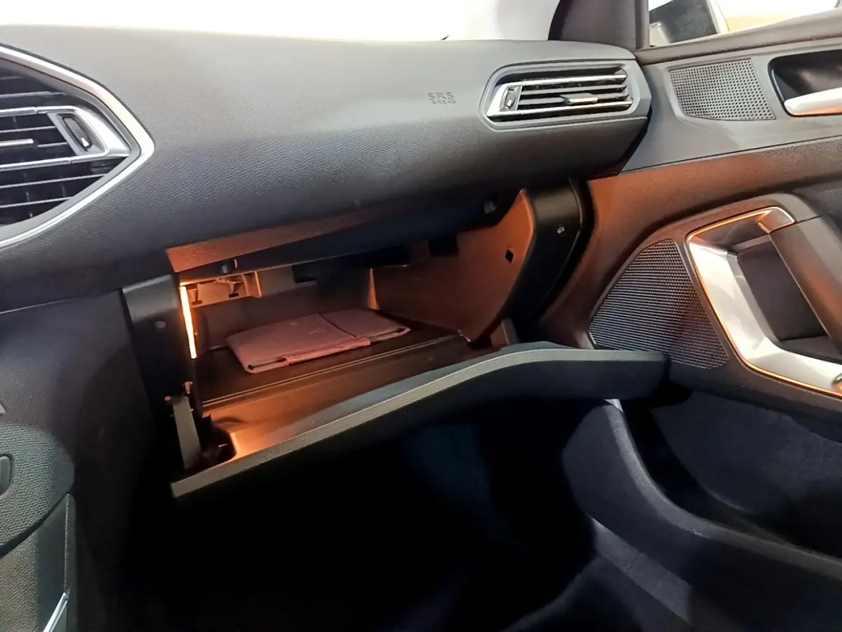 Vue intérieure côté passager de la Peugeot 308 blanche, boîte à gants ouverte avec éclairage intérieur visible.