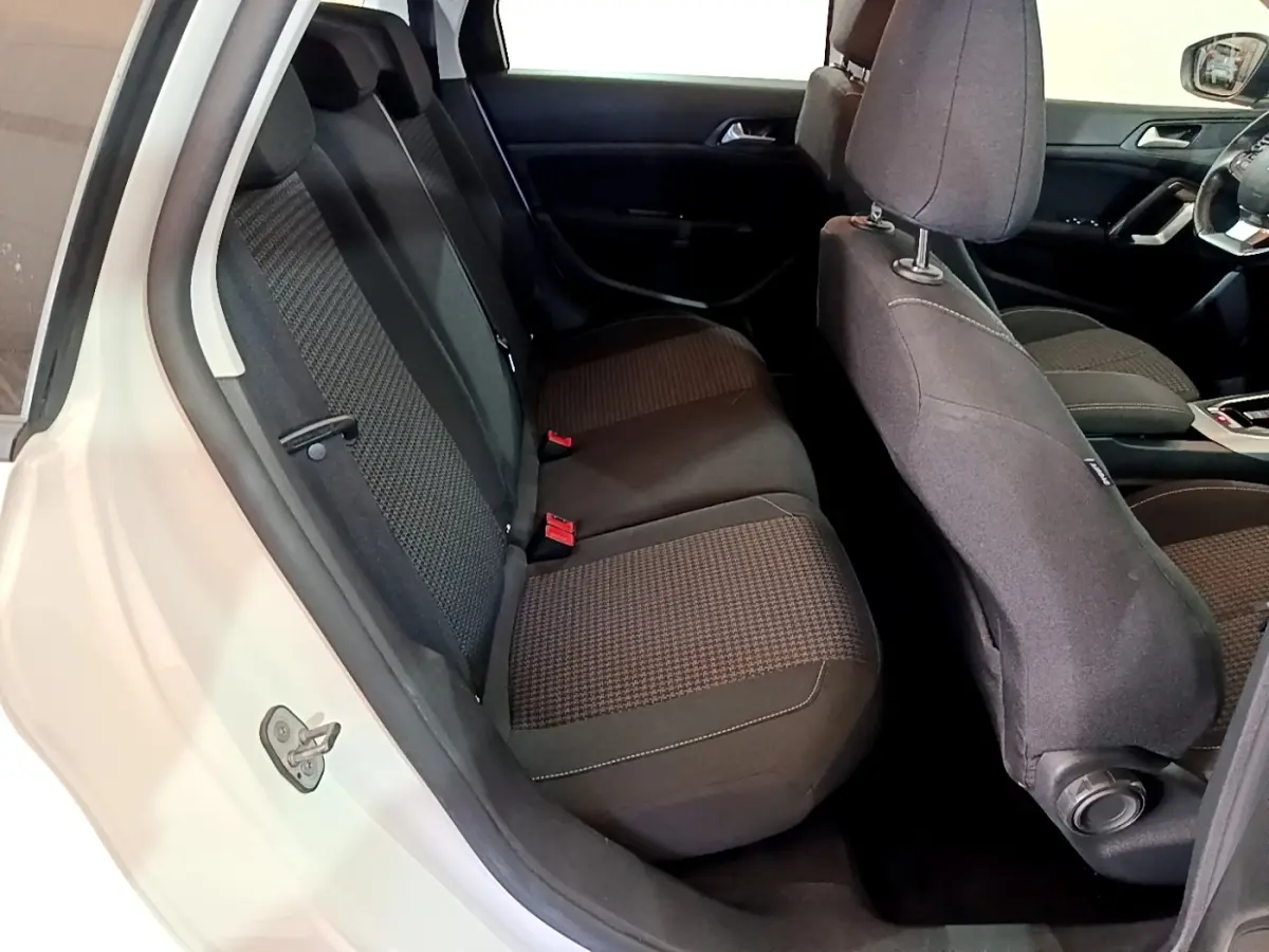 Vue intérieure côté gauche montrant la banquette arrière et les sièges avant noirs d'une Peugeot 308 blanche.