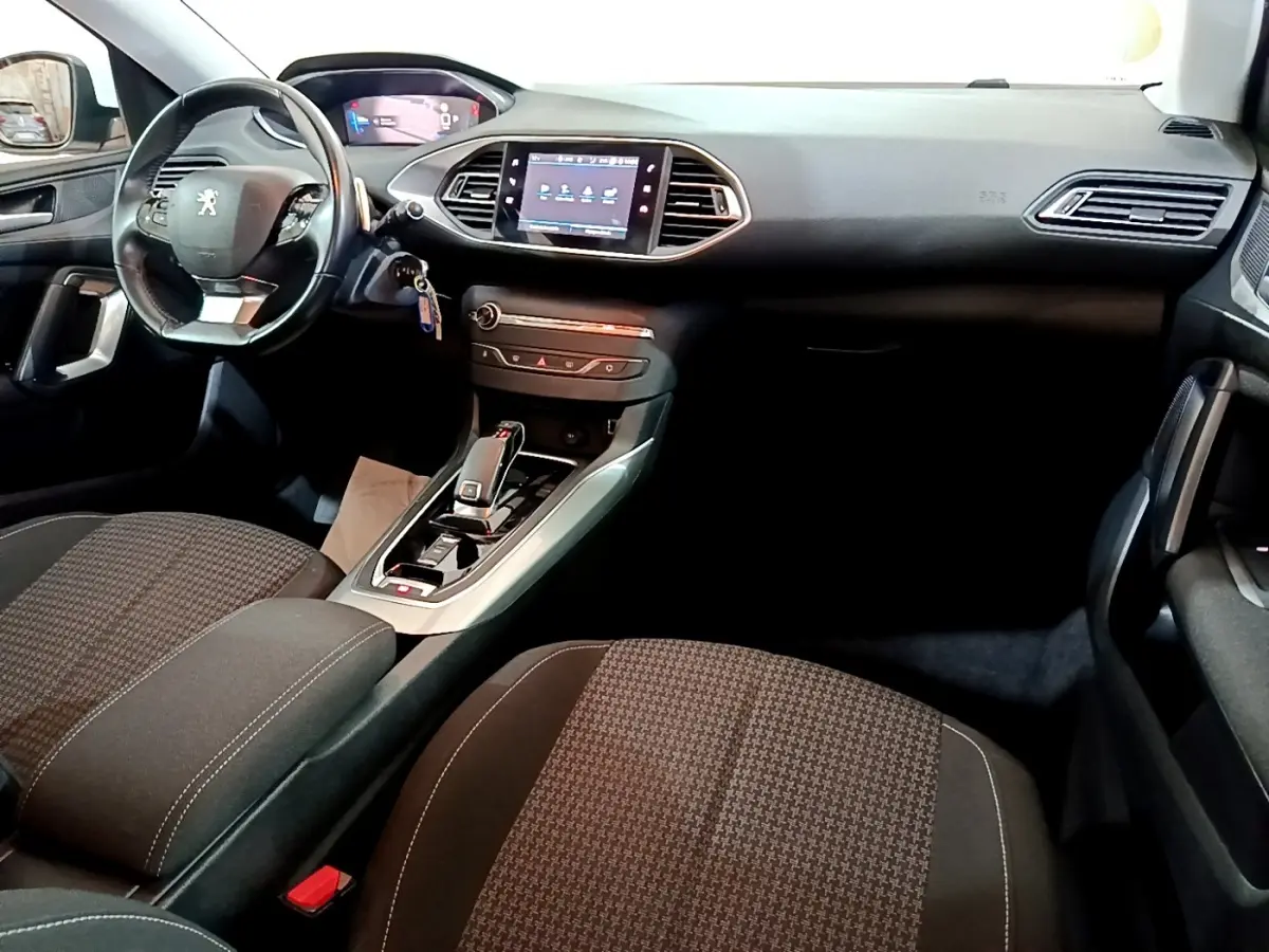 Vue intérieure avant de la Peugeot 308 blanche, montrant le tableau de bord, volant cuir multifonctions et écran tactile central.