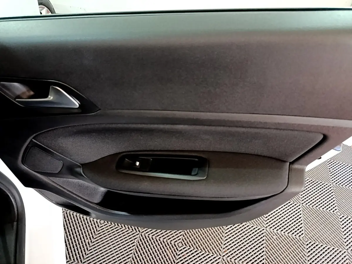 Vue rapprochée de la porte intérieure côté gauche de la Peugeot 308 blanche, avec poignée et commande de vitre noire.