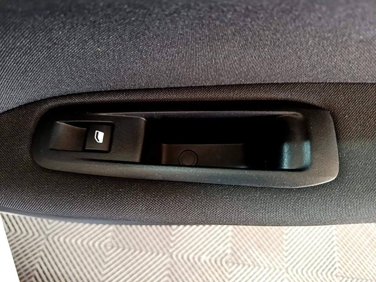 Gros plan sur la poignée intérieure noire avec bouton de lève-vitre sur la porte arrière d’une Peugeot 308 blanche.