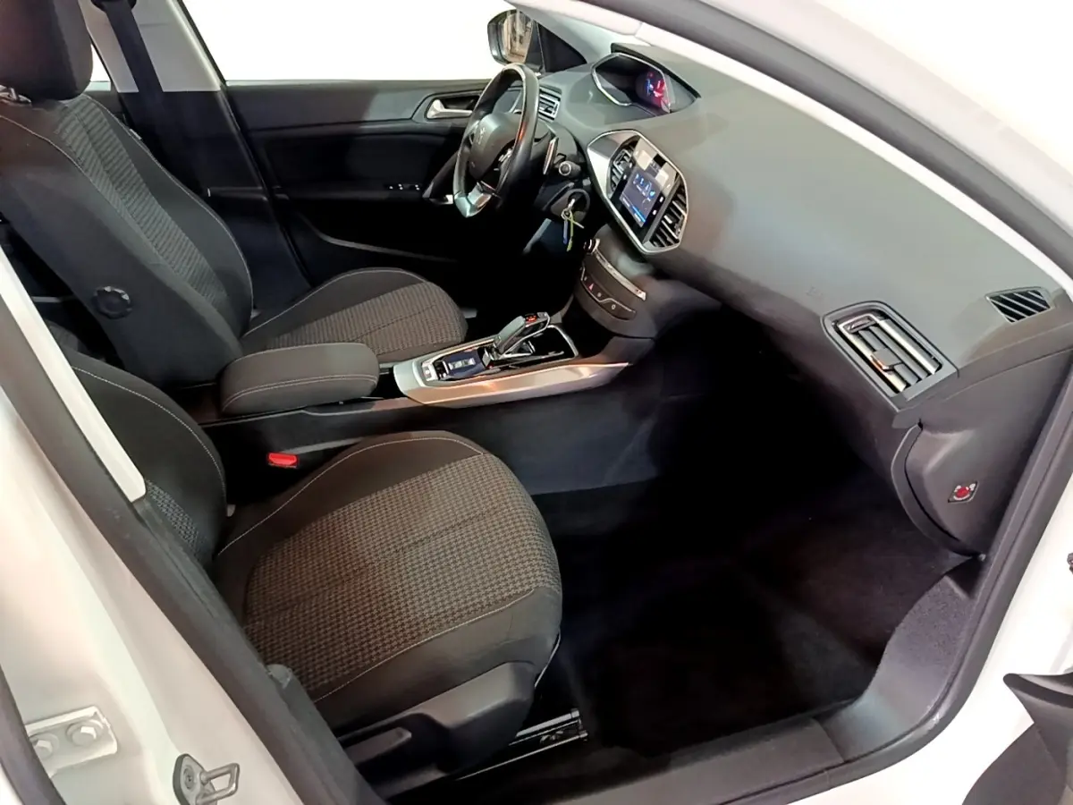 Vue intérieure côté conducteur de la Peugeot 308 blanche, montrant sièges noirs, volant cuir et tableau de bord digital.