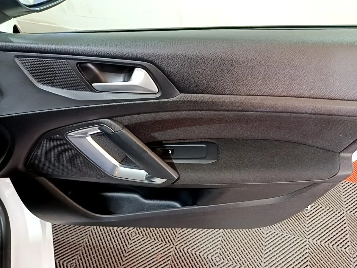 Vue intérieure côté gauche de la porte avant d'une Peugeot 308 blanche, avec poignée argentée et panneau noir.
