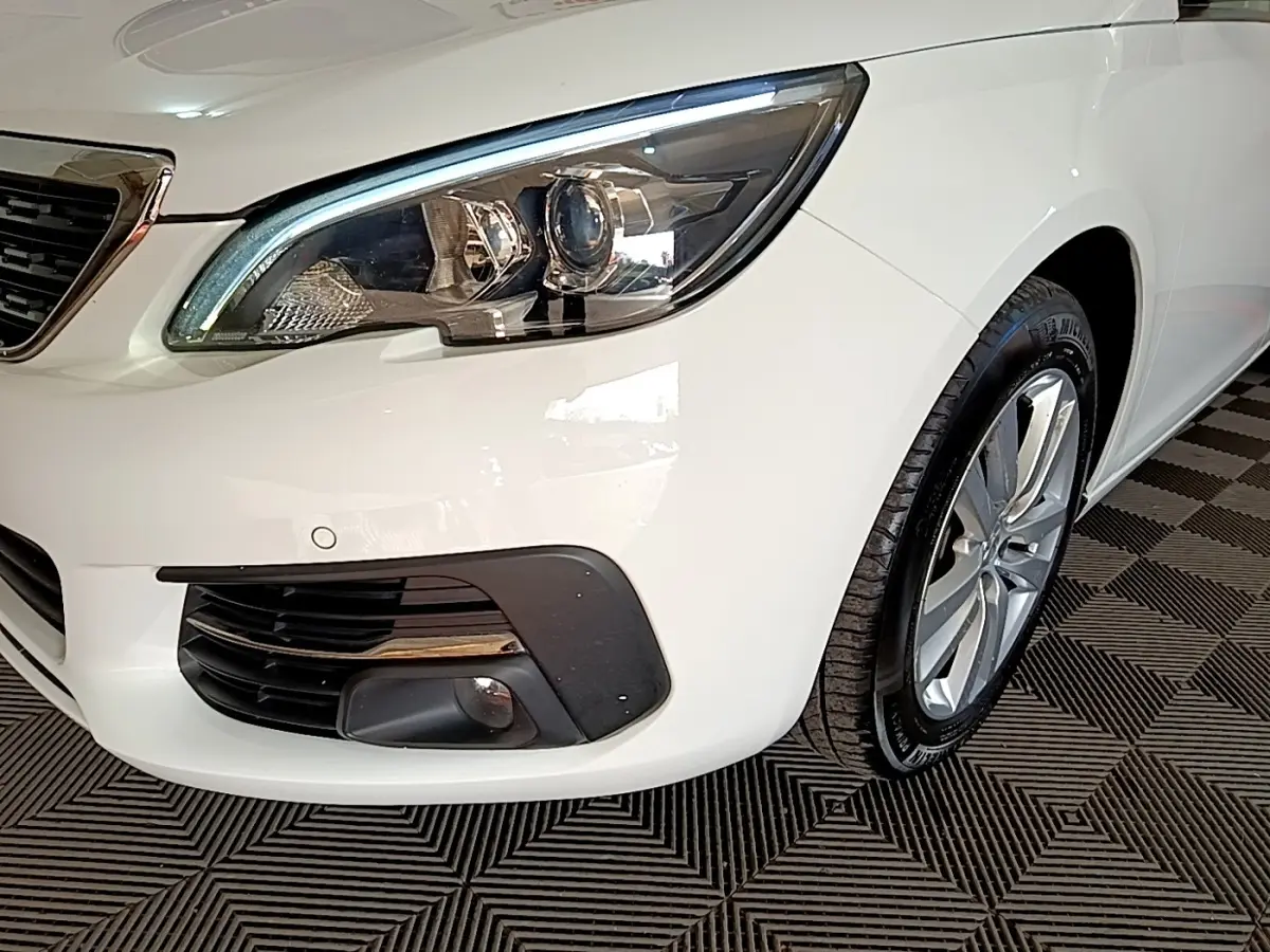 Gros plan sur l'avant droit blanc d'une Peugeot 308 2021, mettant en valeur le phare LED et la roue alliage.