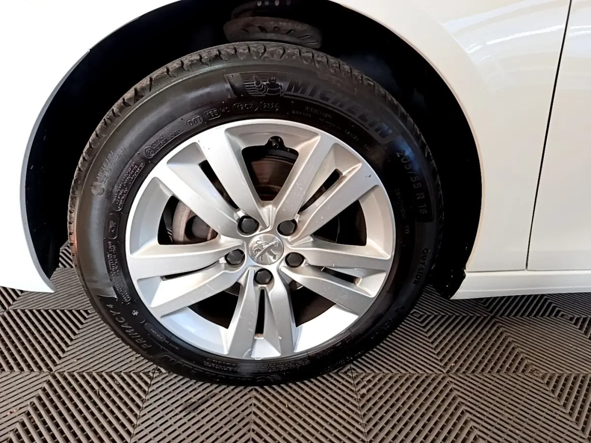 Gros plan sur la roue avant gauche d’une Peugeot 308 blanche, jante alliage et pneu Michelin visibles.
