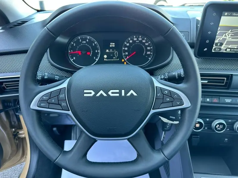 Vue centrée sur le volant noir de la Dacia Sandero beige Safari, avec tableau de bord et écran tactile visibles.