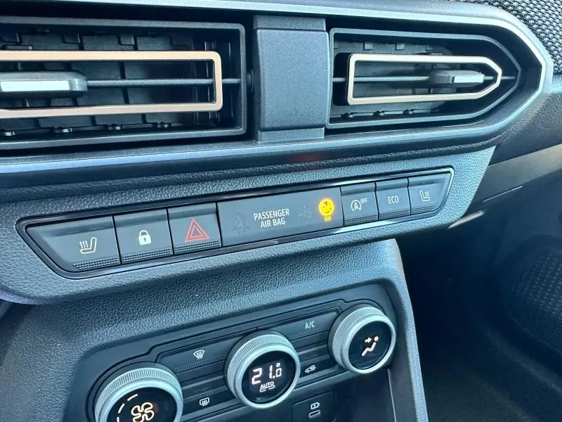 Vue rapprochée de la console centrale noire de la Dacia Sandero beige Safari, montrant les commandes de climatisation et d'airbag passager.