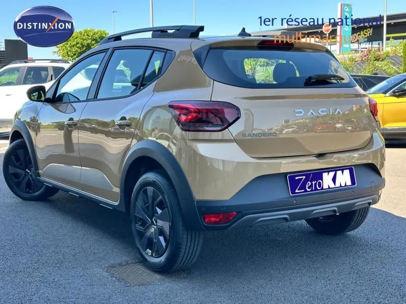 Vue 3/4 arrière droite d'une Dacia Sandero beige Safari avec barres de toit et jantes noires.