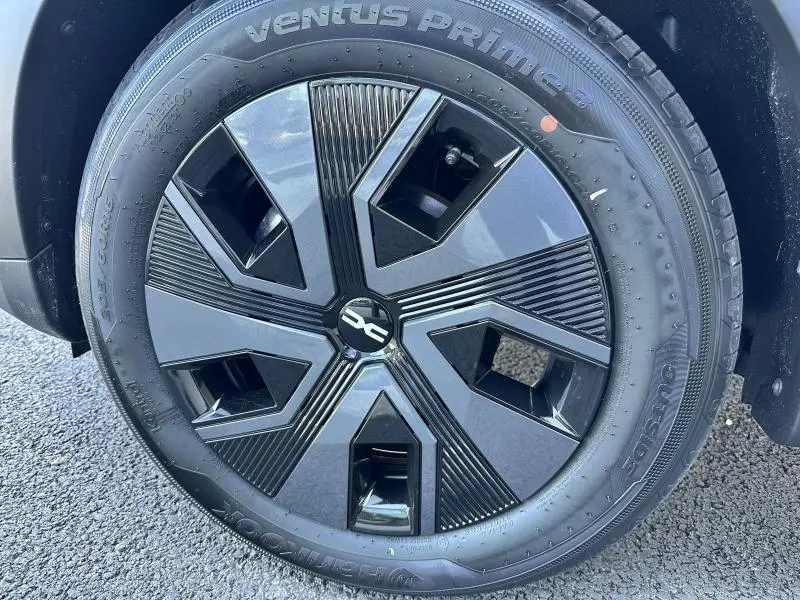 Gros plan sur la roue avant droite de la Dacia Sandero beige Safari, mettant en valeur la jante noire au design géométrique.