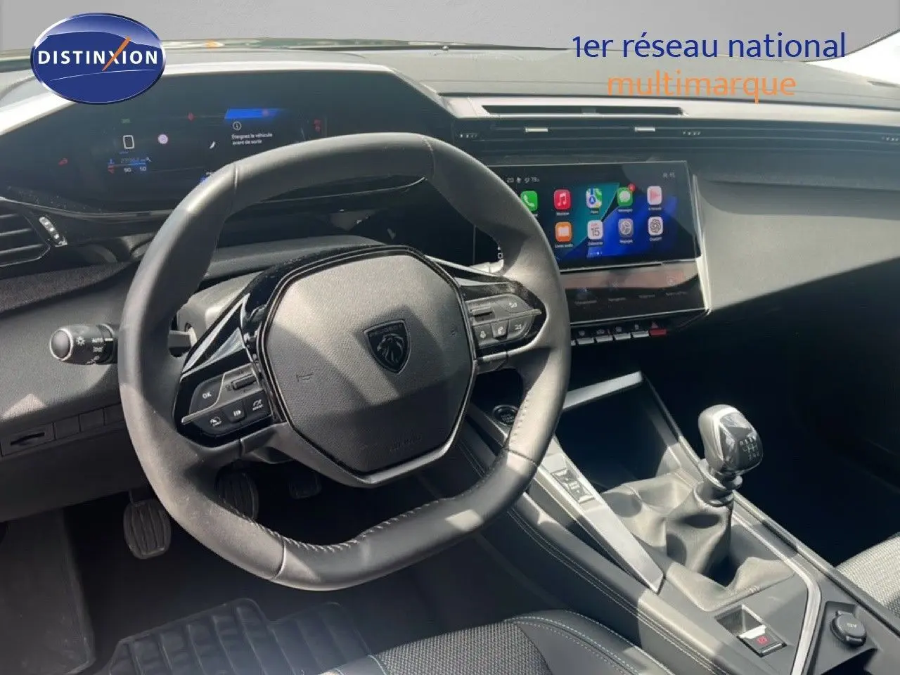 Vue intérieure centrée sur le volant et la console centrale d’une Peugeot 308 2024 avec boîte manuelle, ambiance noire moderne.