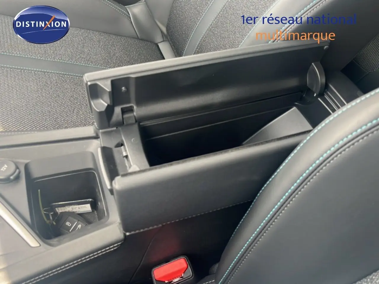 Vue intérieure rapprochée du coffre central ouvert et des sièges tissu gris noir avec surpiqûres bleues d’une Peugeot 308 2024.