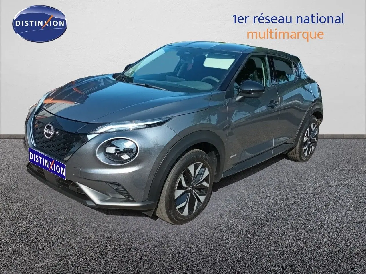 Nissan Juke Hybrid gris squale metal en 3/4 avant droit, avec jantes alliage et calandre noire distinctive.