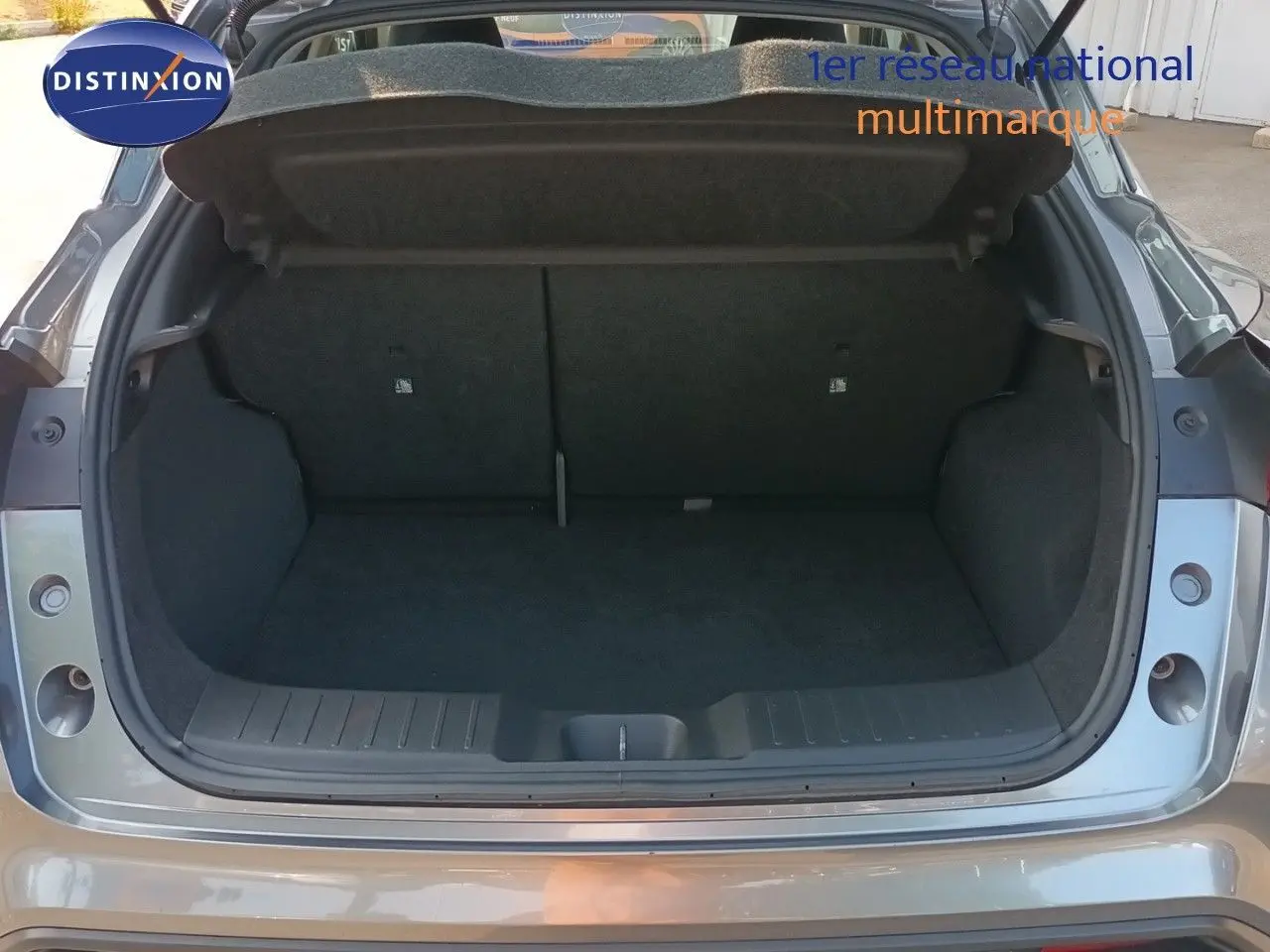 Coffre ouvert vu de l'arrière d'un Nissan Juke 2025 gris squale métal, intérieur de coffre spacieux et propre.