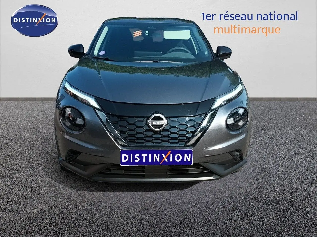 Vue frontale d’un Nissan Juke hybride gris squale métal avec calandre en nid d’abeille et phares ronds distinctifs.