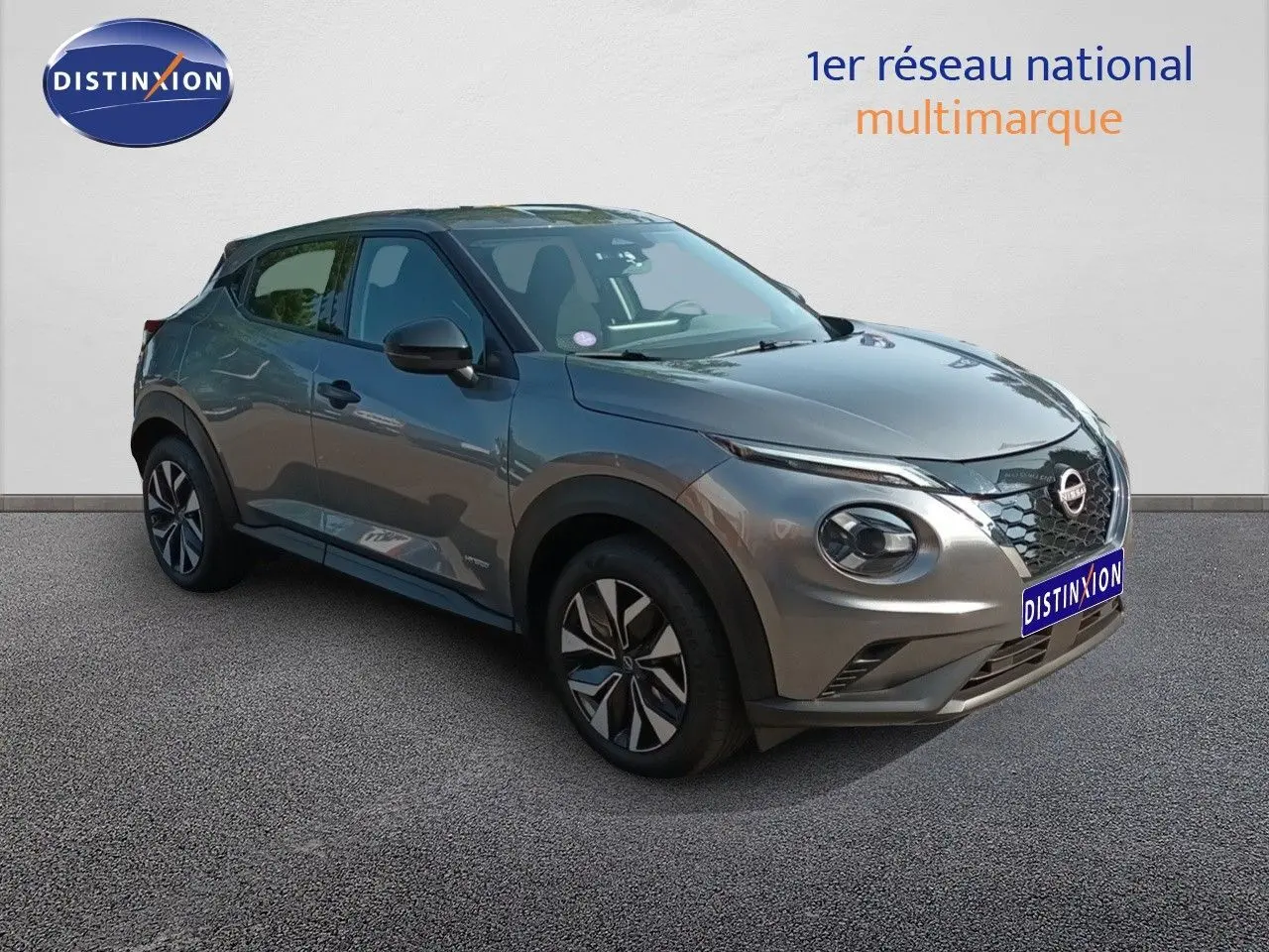 Nissan Juke Hybrid gris squale métal vu en 3/4 avant droit, avec jantes distinctives et calandre noire.