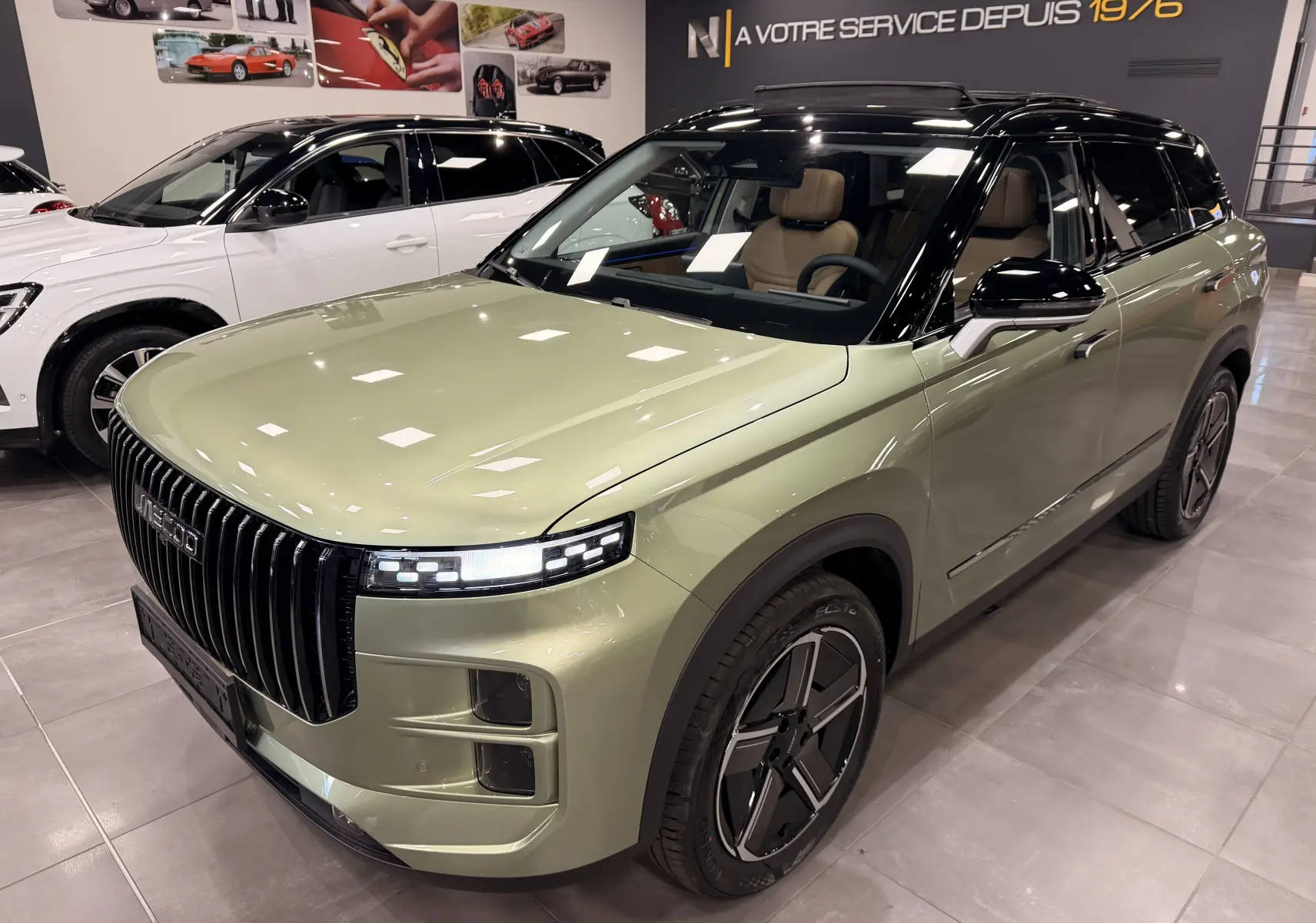 Vue 3/4 avant d’un SUV JAECOO J7 hybride rechargeable gris olive avec toit noir et intérieur cuir brun en showroom.