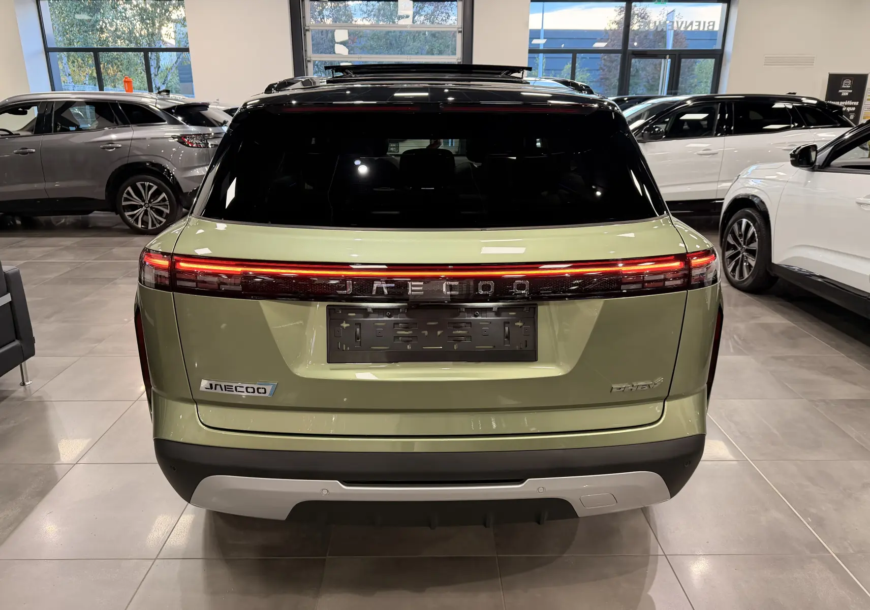 Vue arrière du SUV hybride rechargeable JAECOO J7 gris olive avec feu arrière continu et toit noir en concession.