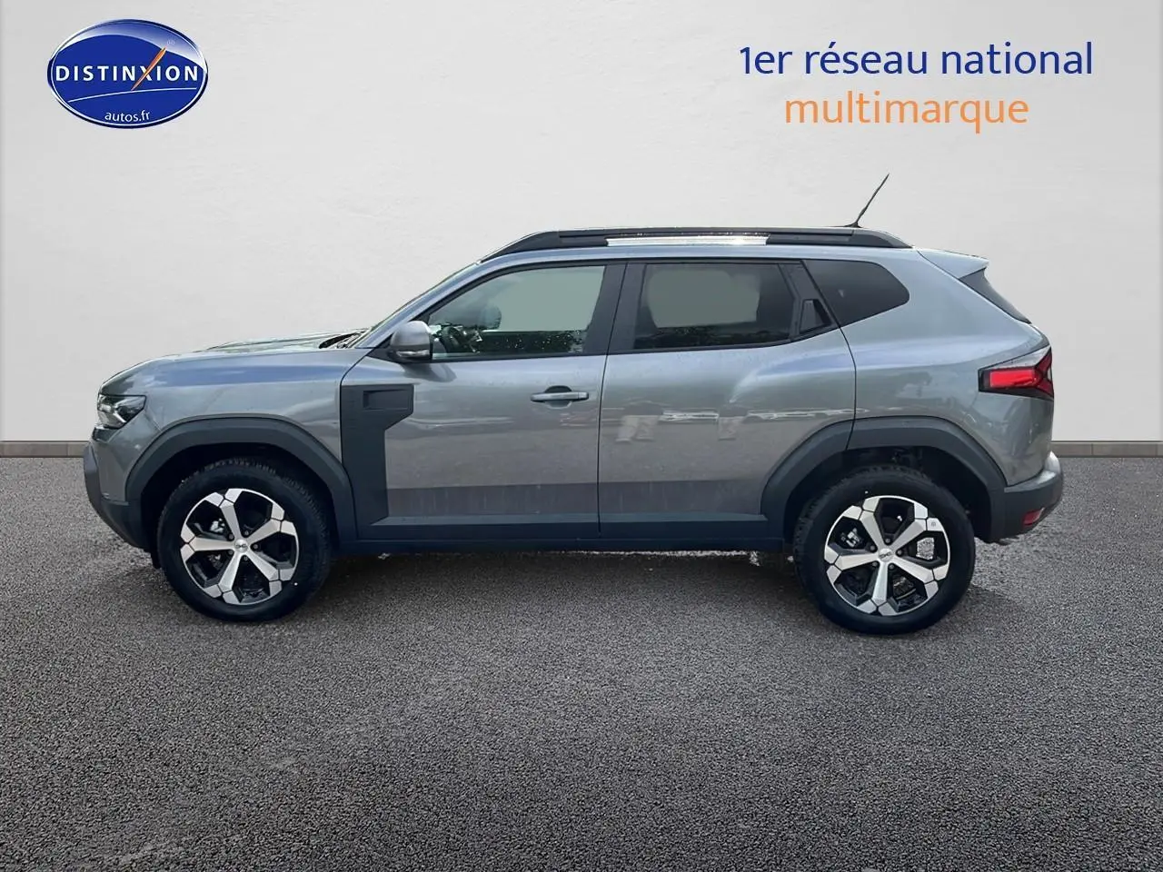 Profil droit du Dacia Duster gris schiste 2025 avec barres de toit et jantes alu distinctives.