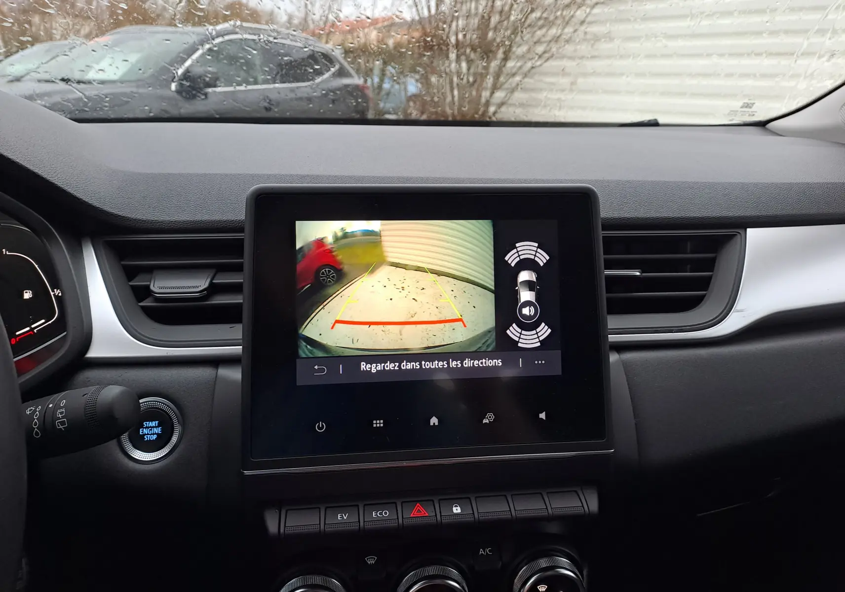Vue intérieure du tableau de bord du Renault Captur gris cassiopée, avec écran de caméra de recul et commandes climatisation visibles.