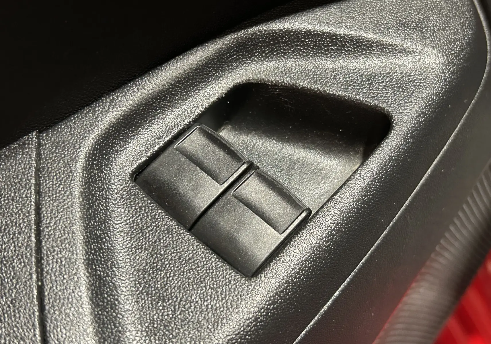Gros plan sur les commandes de lève-vitres côté conducteur dans l’habitacle noir d’une Citroën C1 rouge.