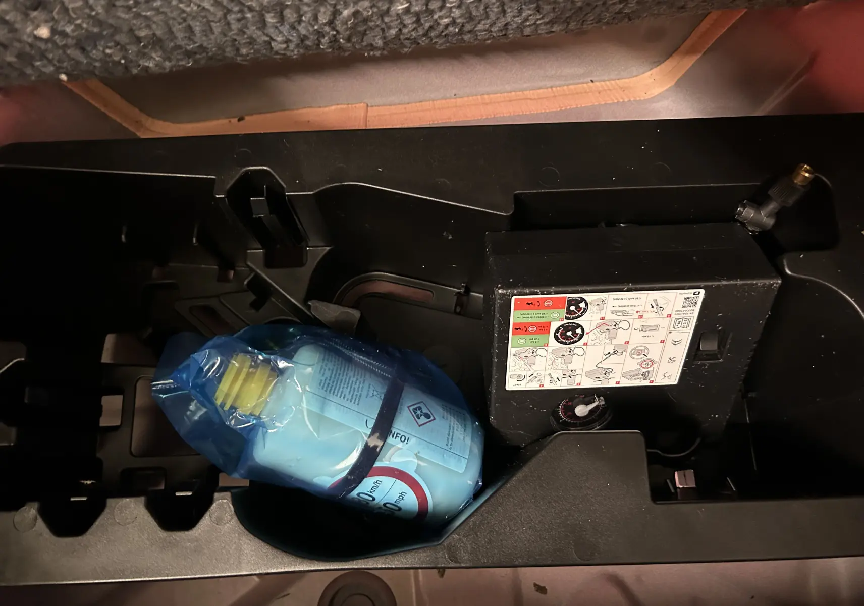 Vue rapprochée de la trousse de réparation pneumatique dans le coffre d'une Citroën C1 rouge, version Airscape 2019.